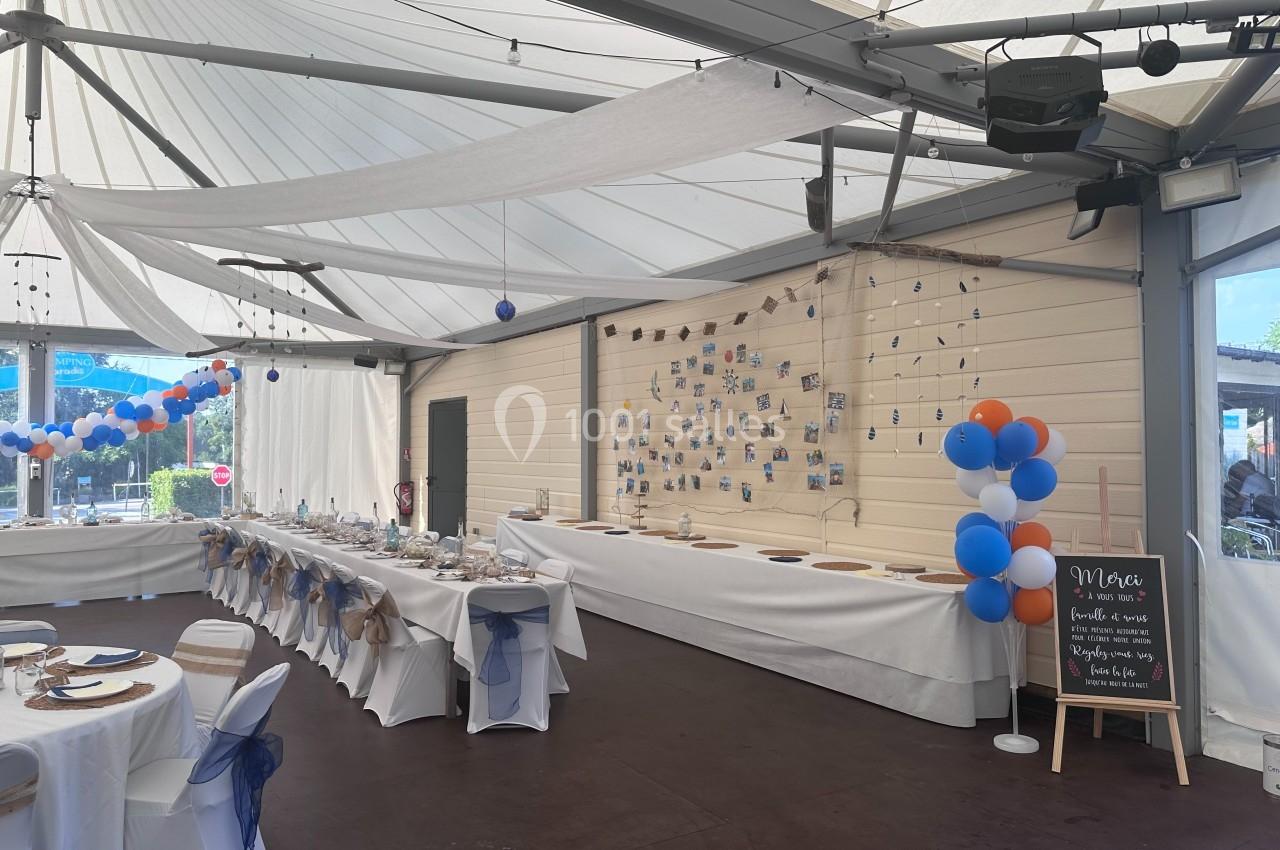 Salle décorée pour un événement avec tables dressées, ballons colorés et panneau d'accueil sur un chevalet.