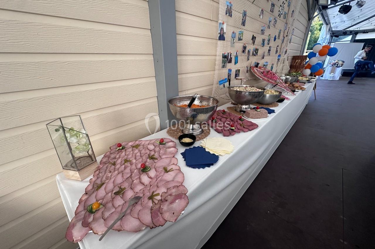 Buffet avec plateaux de charcuterie, bols de salade et décorations sur une table blanche dans un espace couvert.