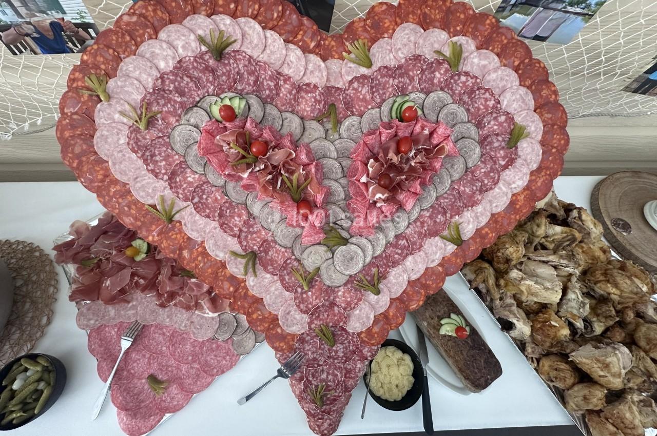 Plateau en forme de cœur composé de charcuteries variées, accompagné de pains, cornichons et poulet rôti.