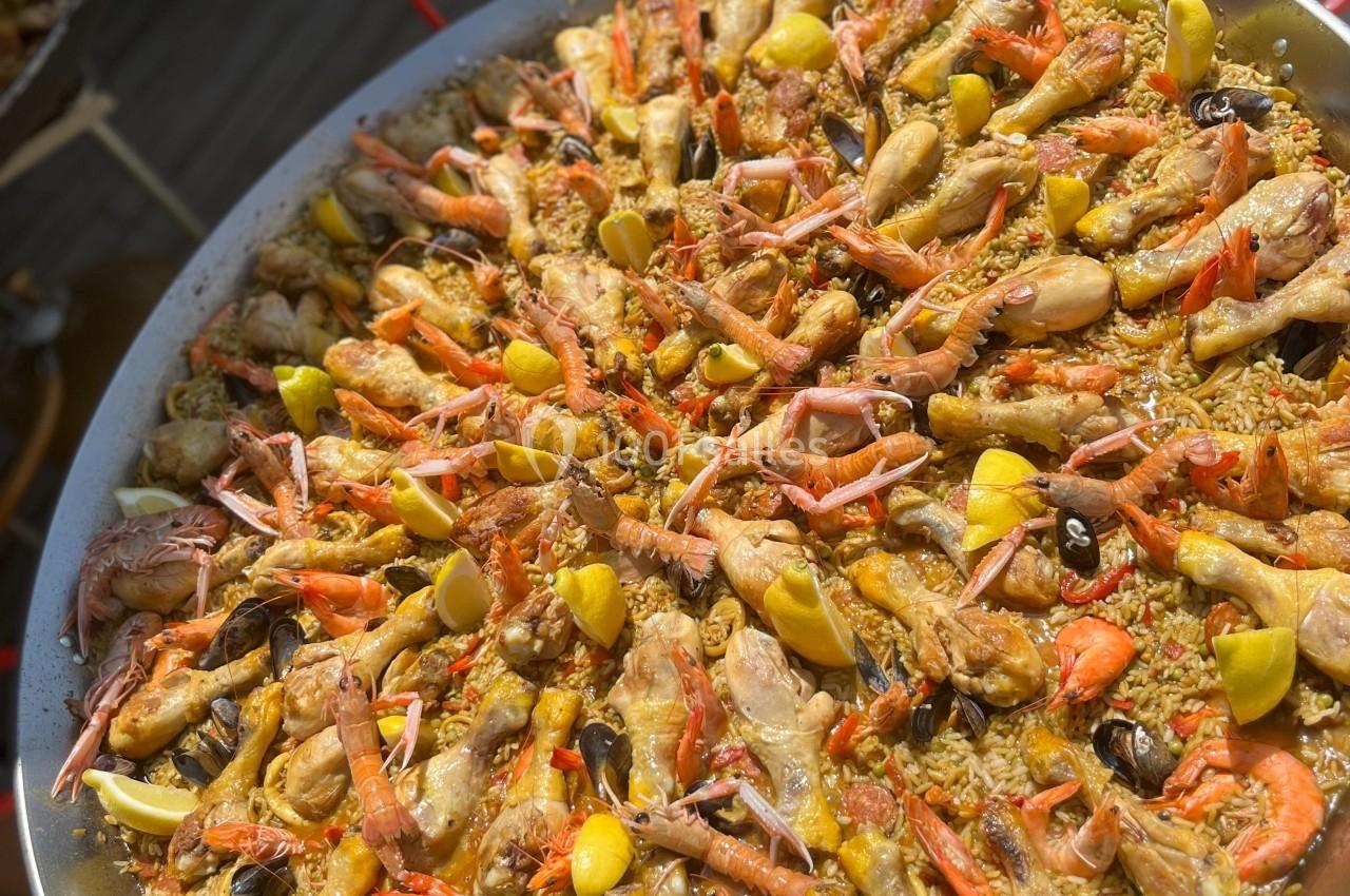 Grande poêle de paella garnie de fruits de mer, morceaux de poulet, légumes et quartiers de citron.