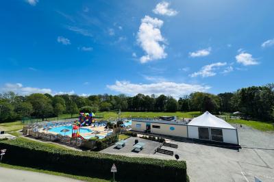 Vue d'un espace extérieur avec piscine, toboggans colorés, pelouse, bâtiment blanc et ciel dégagé.