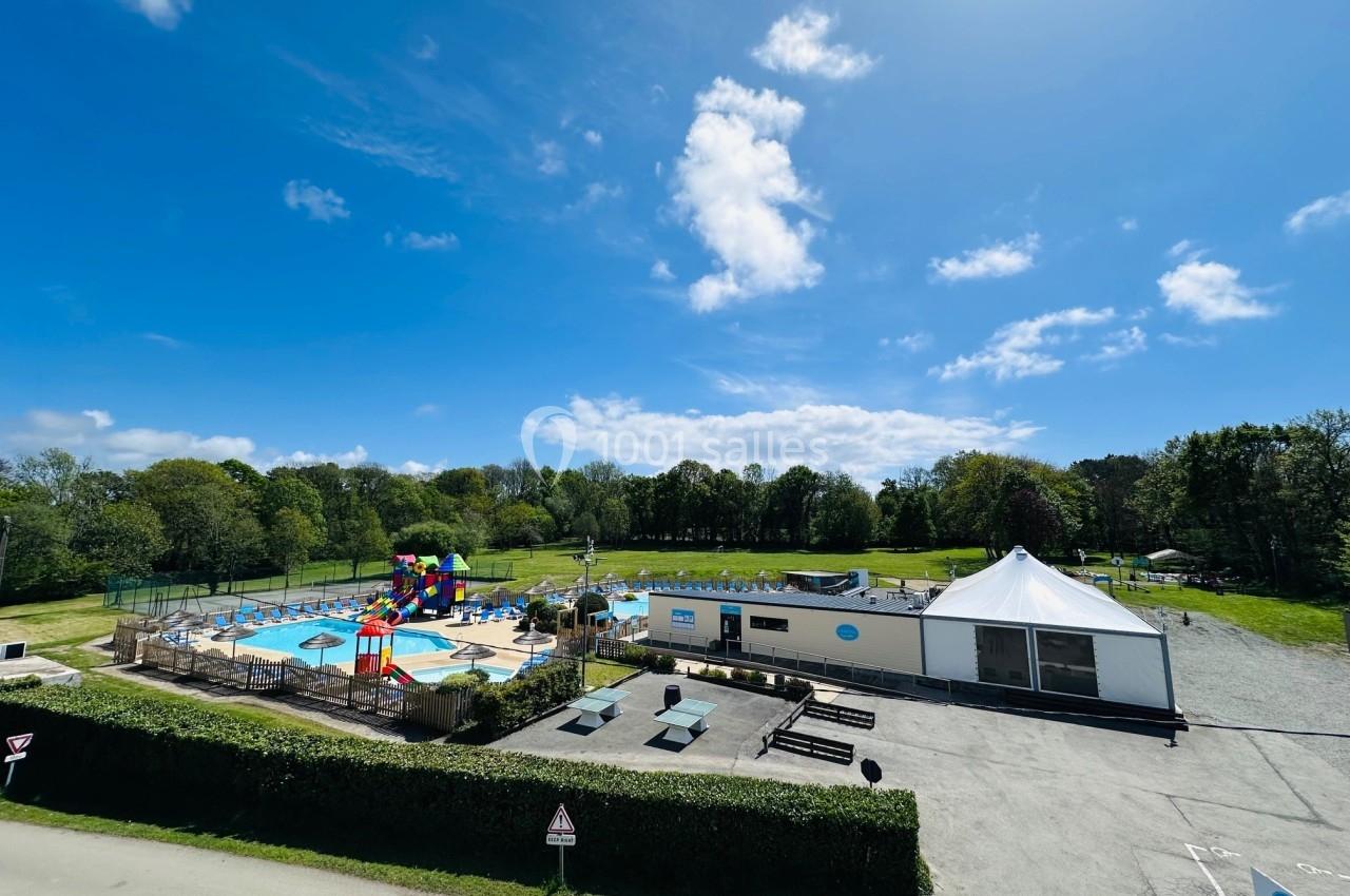 Vue d'un espace extérieur avec piscine, toboggans colorés, pelouse, bâtiment blanc et ciel dégagé.