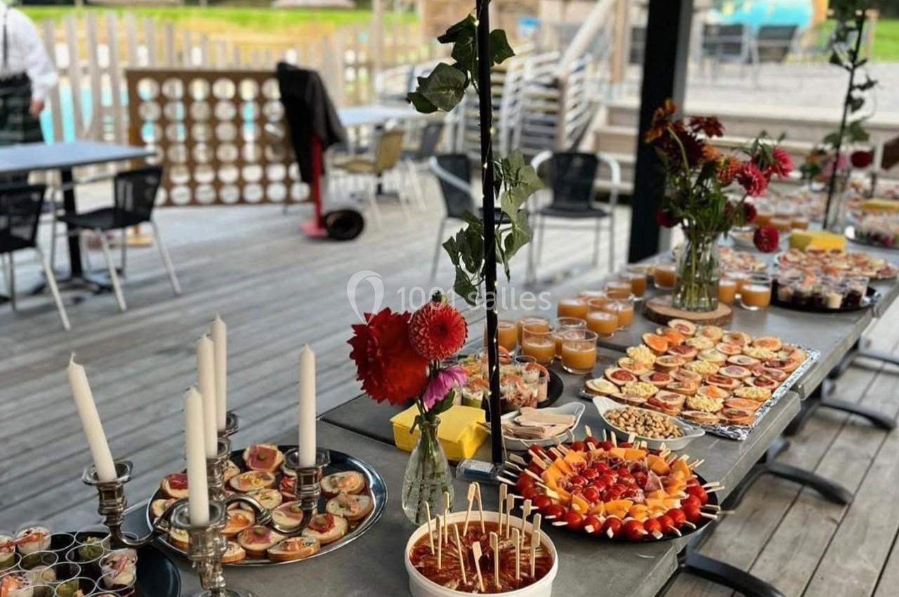 Buffet varié disposé sur une table en extérieur, avec fleurs décoratives et vue sur une terrasse en bois.