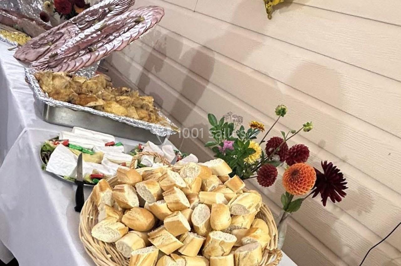 Plateau de petits pains, plats de viande et charcuterie sur une table décorée de fleurs pour un buffet.