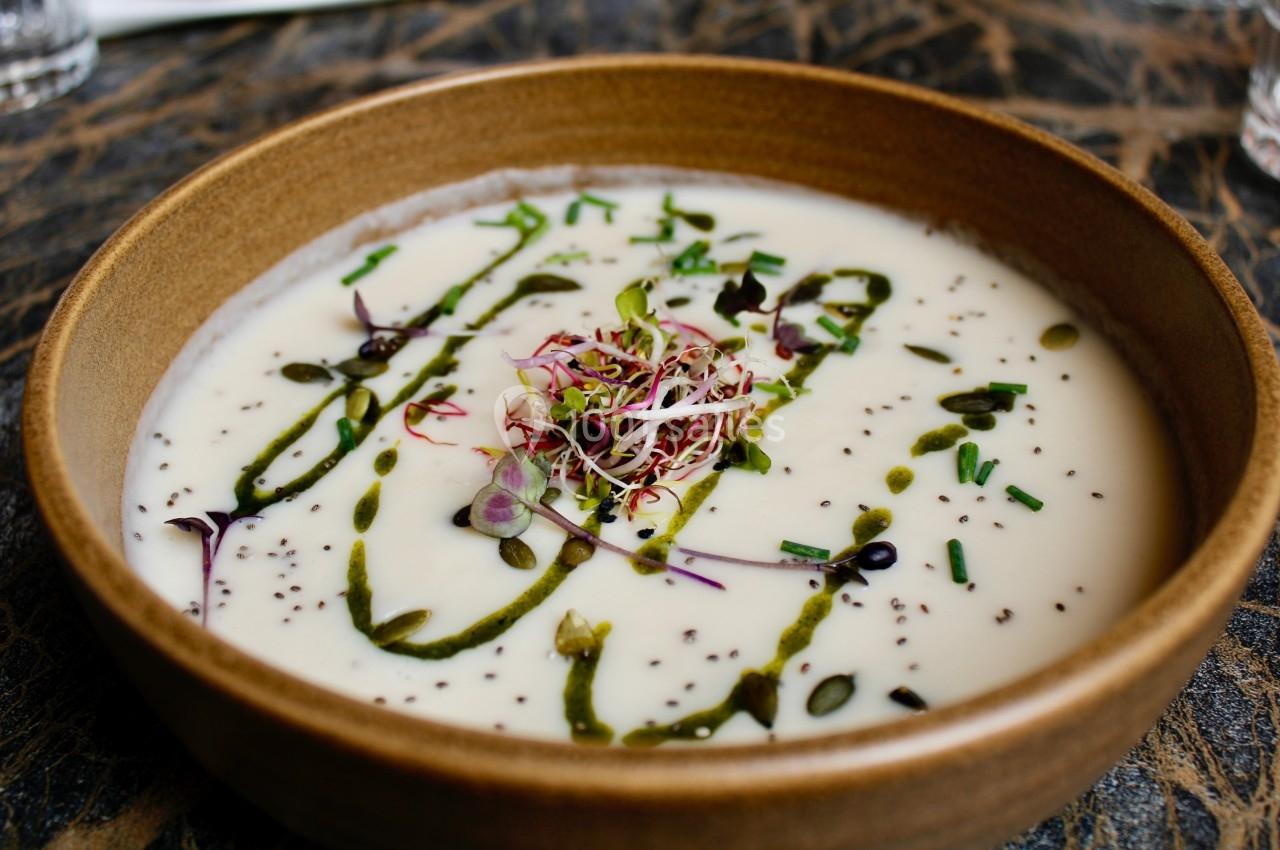 Bol de soupe crémeuse garnie de graines, herbes fraîches et filet d'huile verte sur une table en pierre.