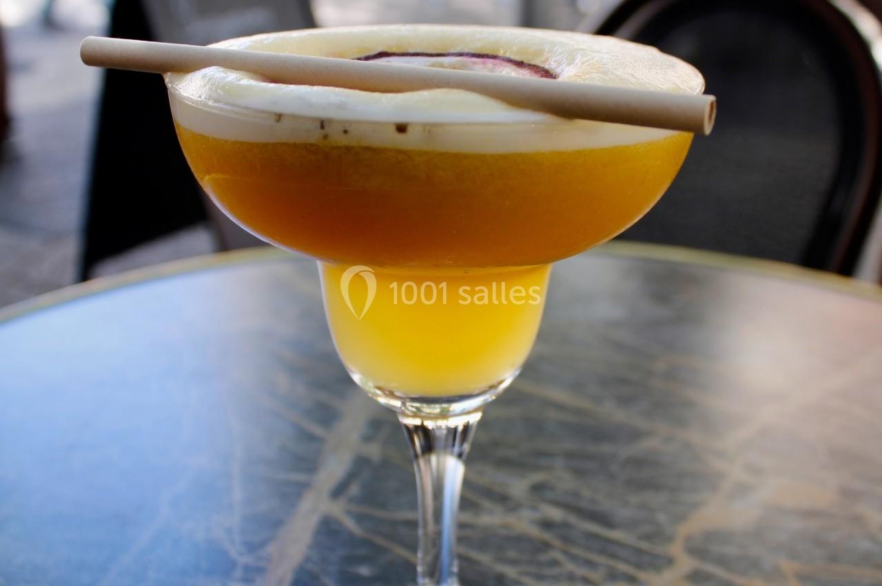 Verre à cocktail jaune sur une table en marbre, garni de mousse, d'une tranche de fruit et d'une paille.