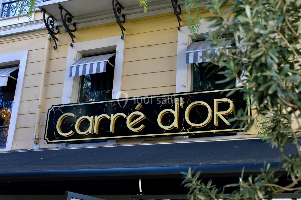 Enseigne noire et dorée indiquant ’Carré d'Or’ sur la façade d'un bâtiment jaune avec des fenêtres à stores rayés.