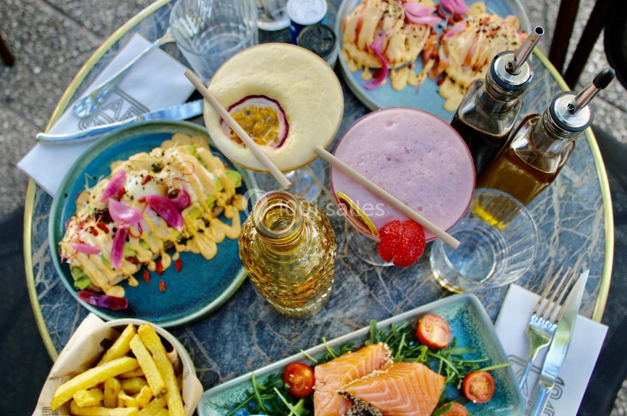 Table avec des plats variés : saumon, frites, wraps, smoothies et condiments, disposés sur une table en extérieur.