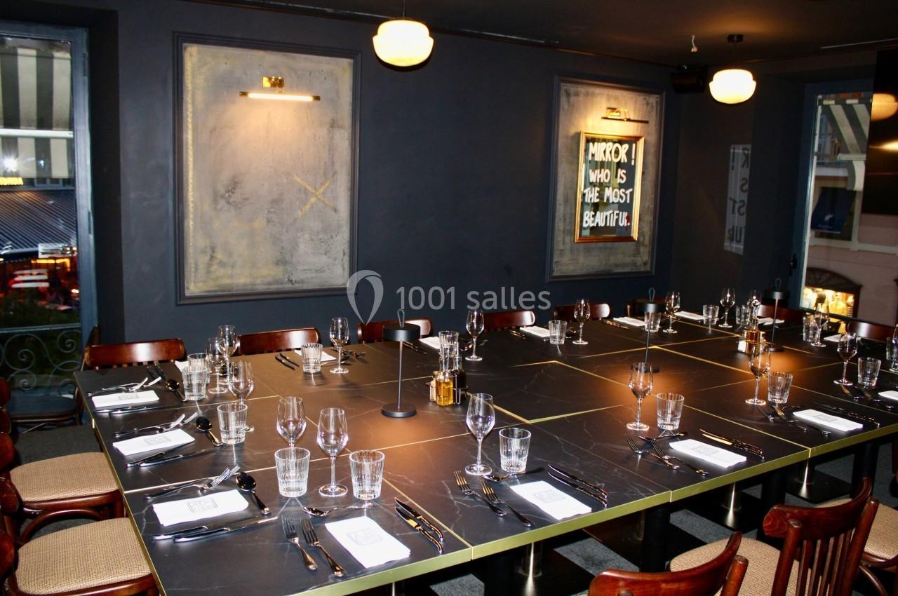 Salle à manger élégante avec une grande table rectangulaire dressée, entourée de chaises en bois, éclairée par des…