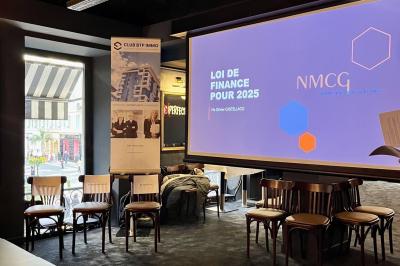Salle de réunion moderne avec tables disposées en U, chaises en bois, éclairage suspendu et écran mural.