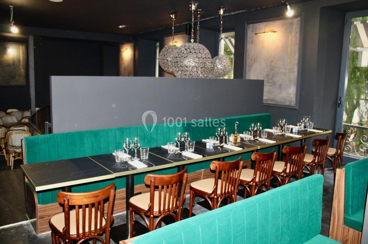 Salle de restaurant avec banquettes vertes, chaises en bois, tables dressées et luminaires modernes suspendus.