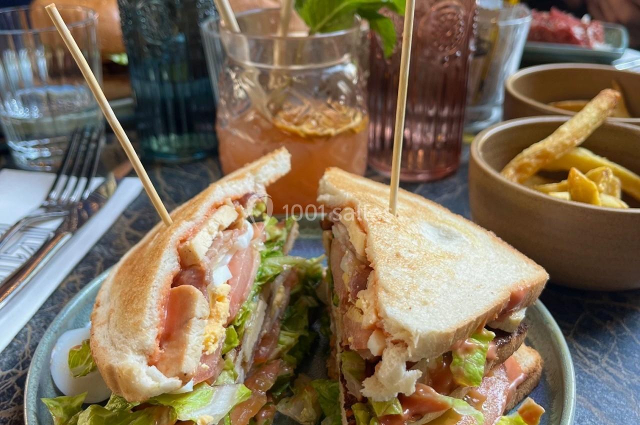 Sandwich club garni de salade, tomate et poulet, accompagné de frites et d'une boisson sur une table de restaurant.