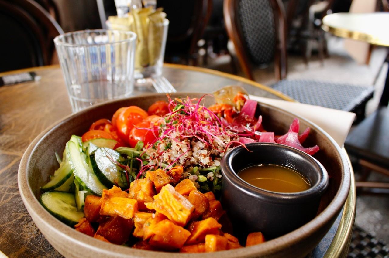 Bol de légumes colorés avec patate douce, concombre, tomates, quinoa, germes et une sauce servie à part.