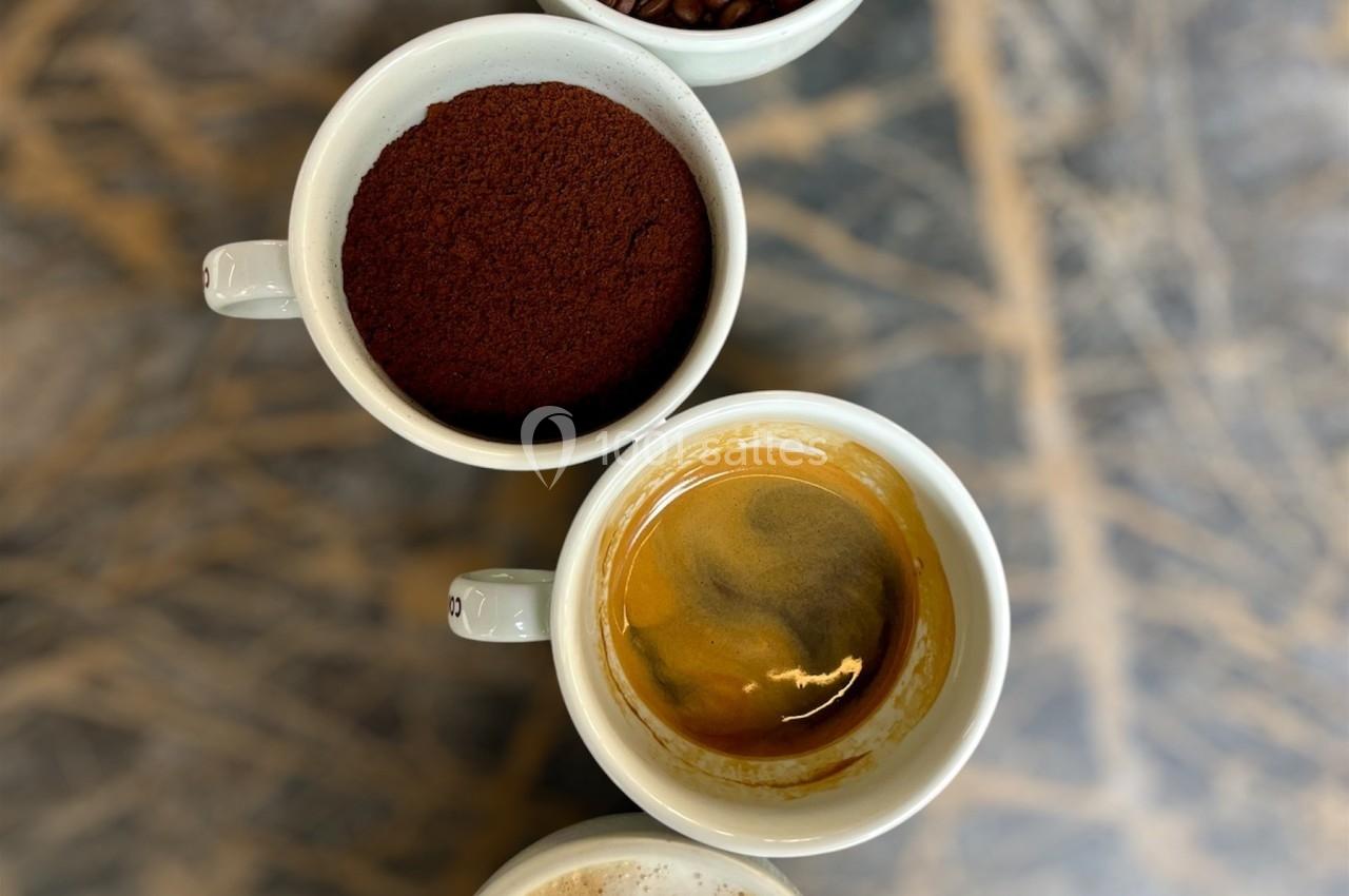 Quatre tasses alignées contenant des grains de café, du café moulu, un espresso et un cappuccino avec un motif en cœur.