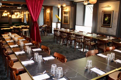 Salle de réunion moderne avec tables disposées en U, chaises en bois, éclairage suspendu et écran mural.