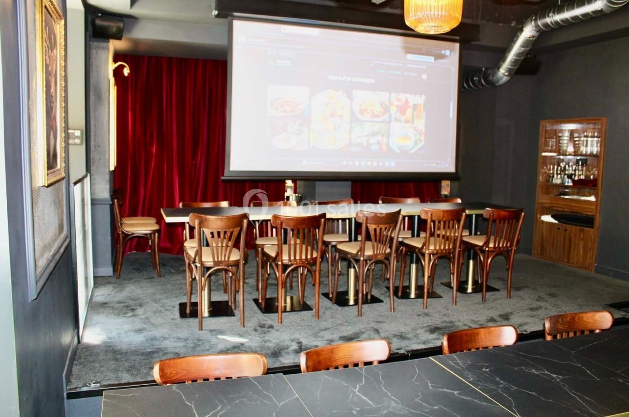 Salle équipée d'un projecteur, avec des chaises en bois alignées devant un écran et un rideau rouge en arrière-plan.