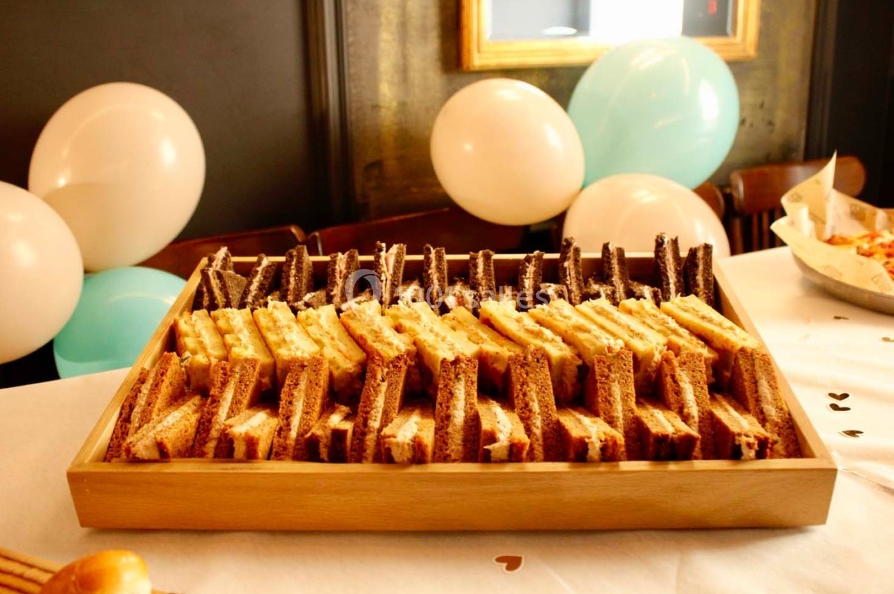 Plateau en bois contenant des sandwichs triangulaires alignés, avec des ballons blancs et bleus en arrière-plan.