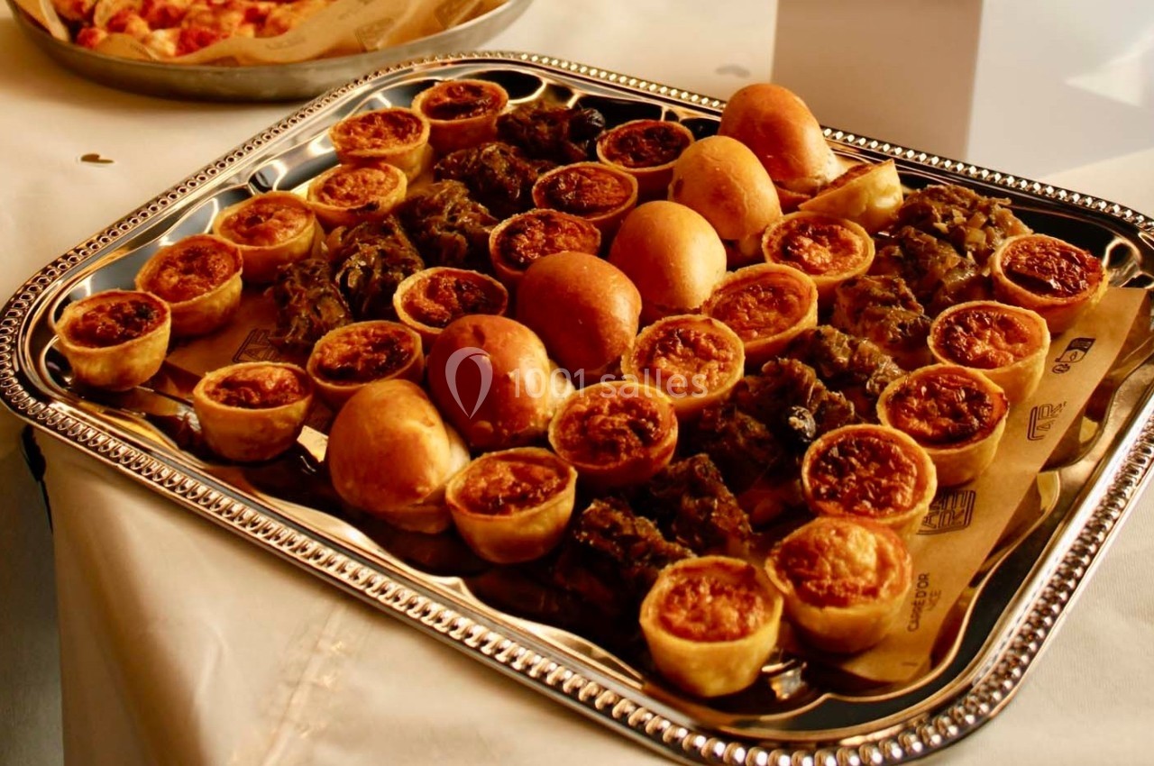 Plateau de mini-quiches, petits pains et bouchées apéritives disposé sur une table recouverte d'une nappe blanche.