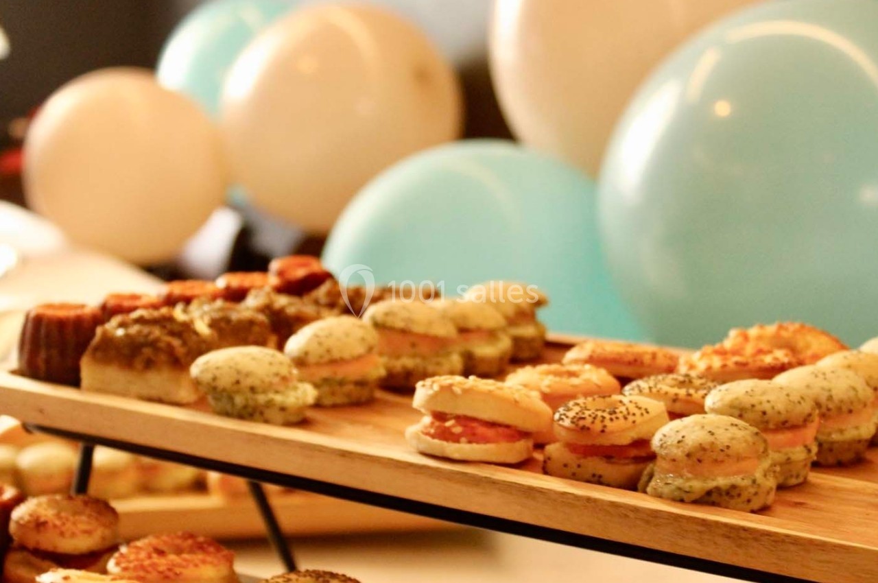 Plateau de mini-sandwichs et amuse-bouches variés, disposé devant des ballons blancs et bleus en arrière-plan.