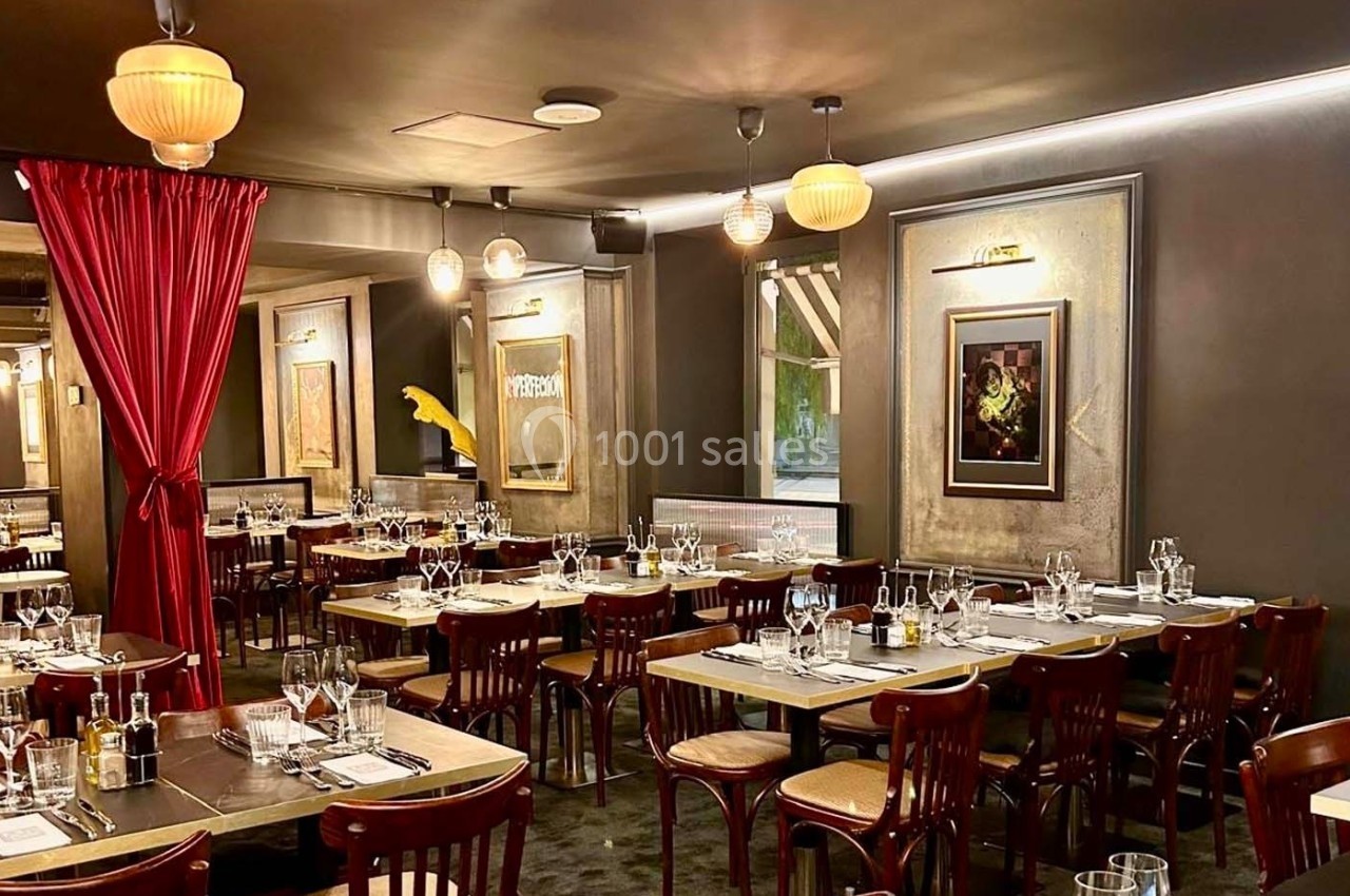 Salle de restaurant élégante avec tables dressées, chaises en bois, rideau rouge et éclairage chaleureux.