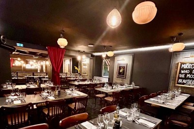 Salle de réunion moderne avec tables disposées en U, chaises en bois, éclairage suspendu et écran mural.
