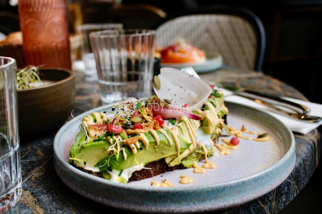 Tartine garnie d'avocat, graines, légumes croquants et sauce, servie dans une assiette sur une table dressée.