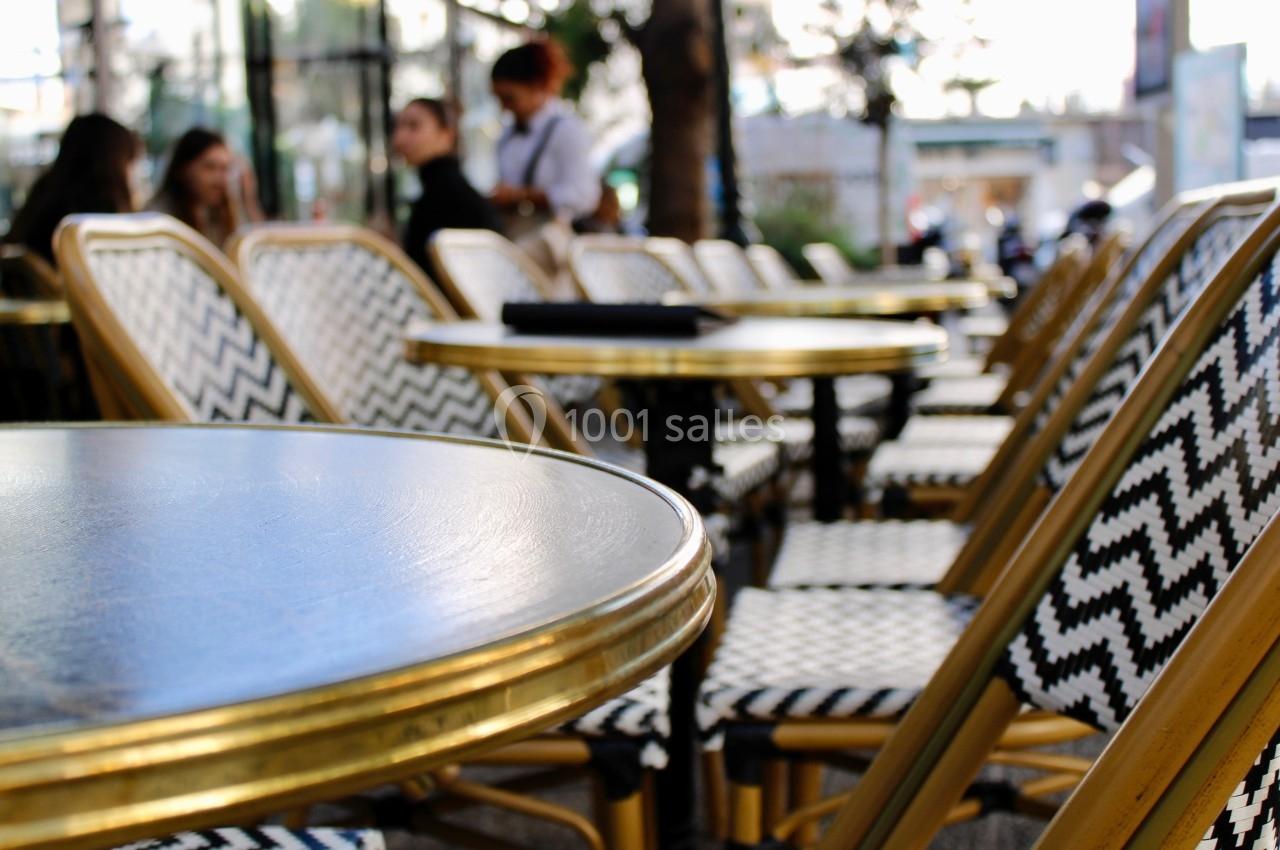 Chaises et tables en terrasse d'un café, avec des motifs géométriques sur les assises et un arrière-plan flou.