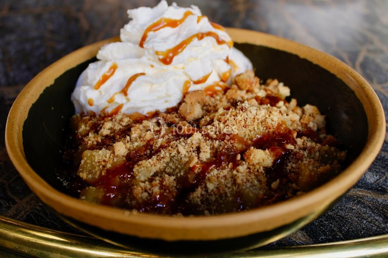 Dessert dans un bol avec crumble, compote de fruits, chantilly et filet de caramel sur une table sombre.