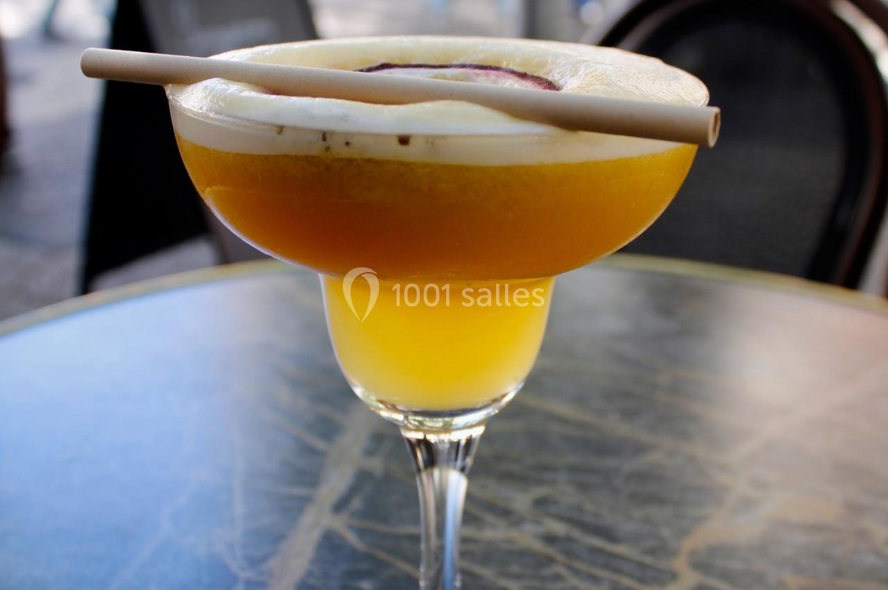 Verre de cocktail jaune sur une table en marbre, garni de mousse et d'une décoration en bois, en extérieur.