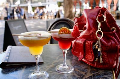 Deux verres de jus colorés sur une table en terrasse, l'un décoré de menthe et d'une tranche d'orange séchée.