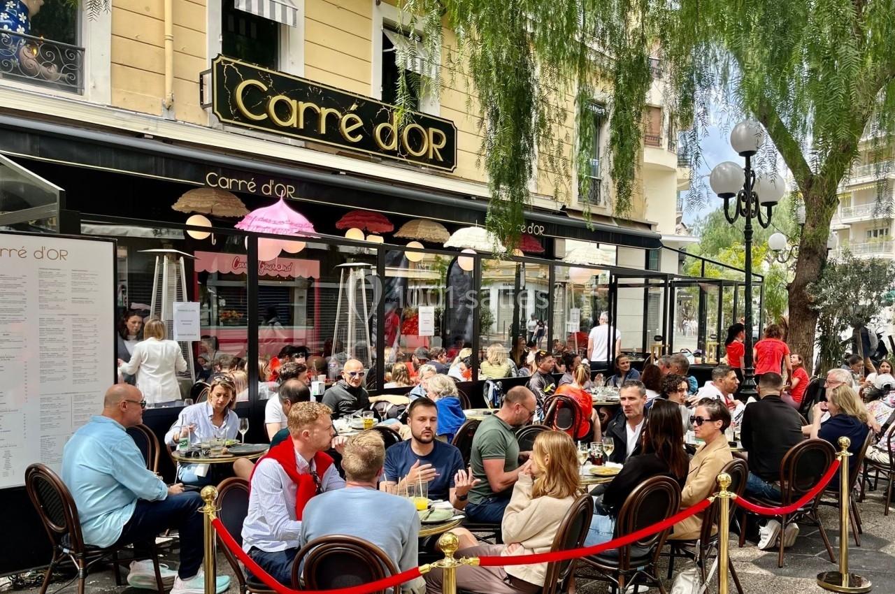 Terrasse animée d'un café-restaurant avec des clients attablés sous un ciel dégagé, devant une façade jaune.