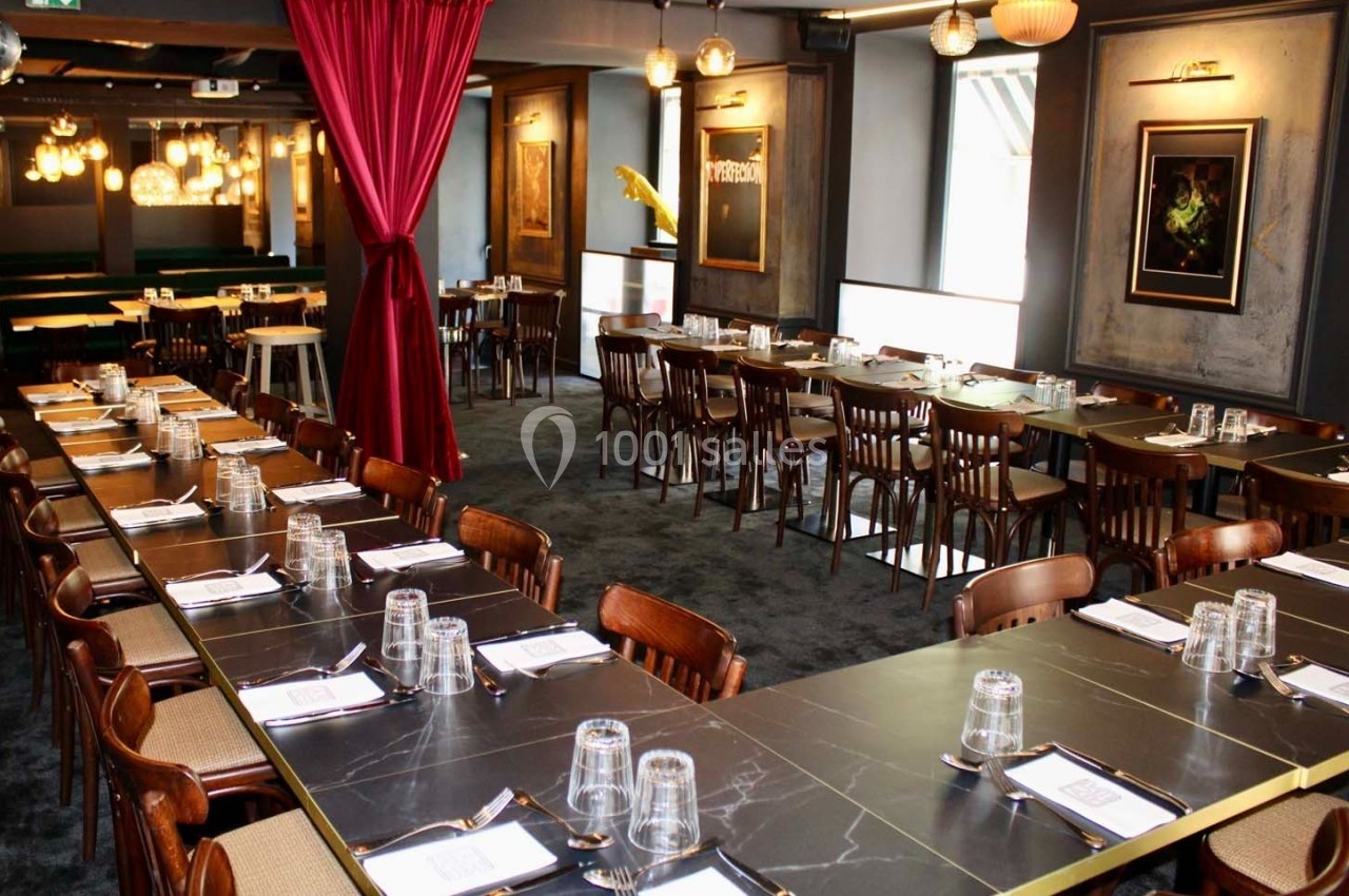 Salle de restaurant élégante avec de longues tables dressées, des chaises en bois et une décoration lumineuse.