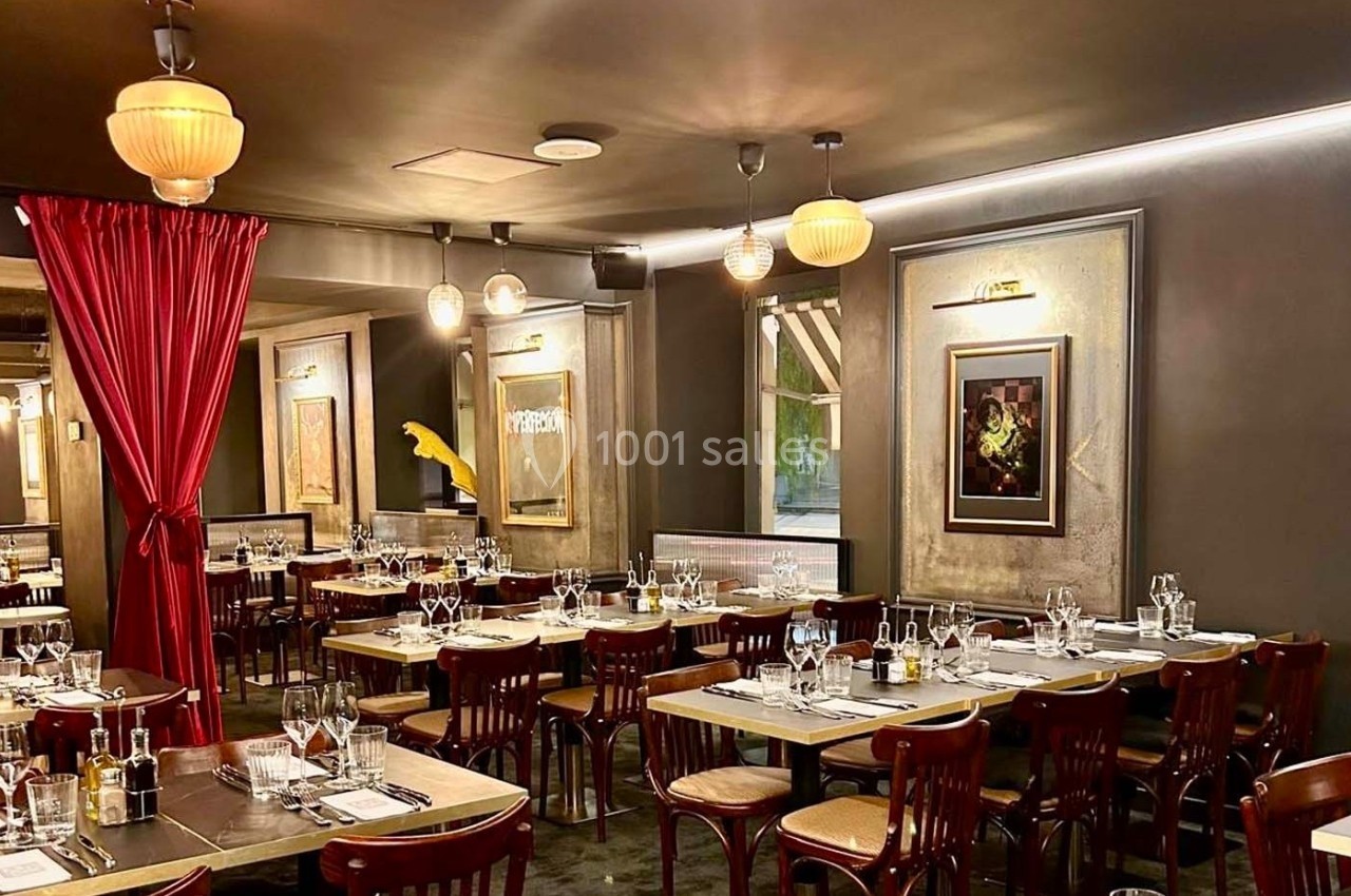 Salle de restaurant élégante avec tables dressées, chaises en bois, rideaux rouges et éclairage chaleureux.