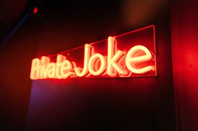 Enseigne lumineuse rouge avec l'inscription ’Private Joke’ dans un environnement sombre.