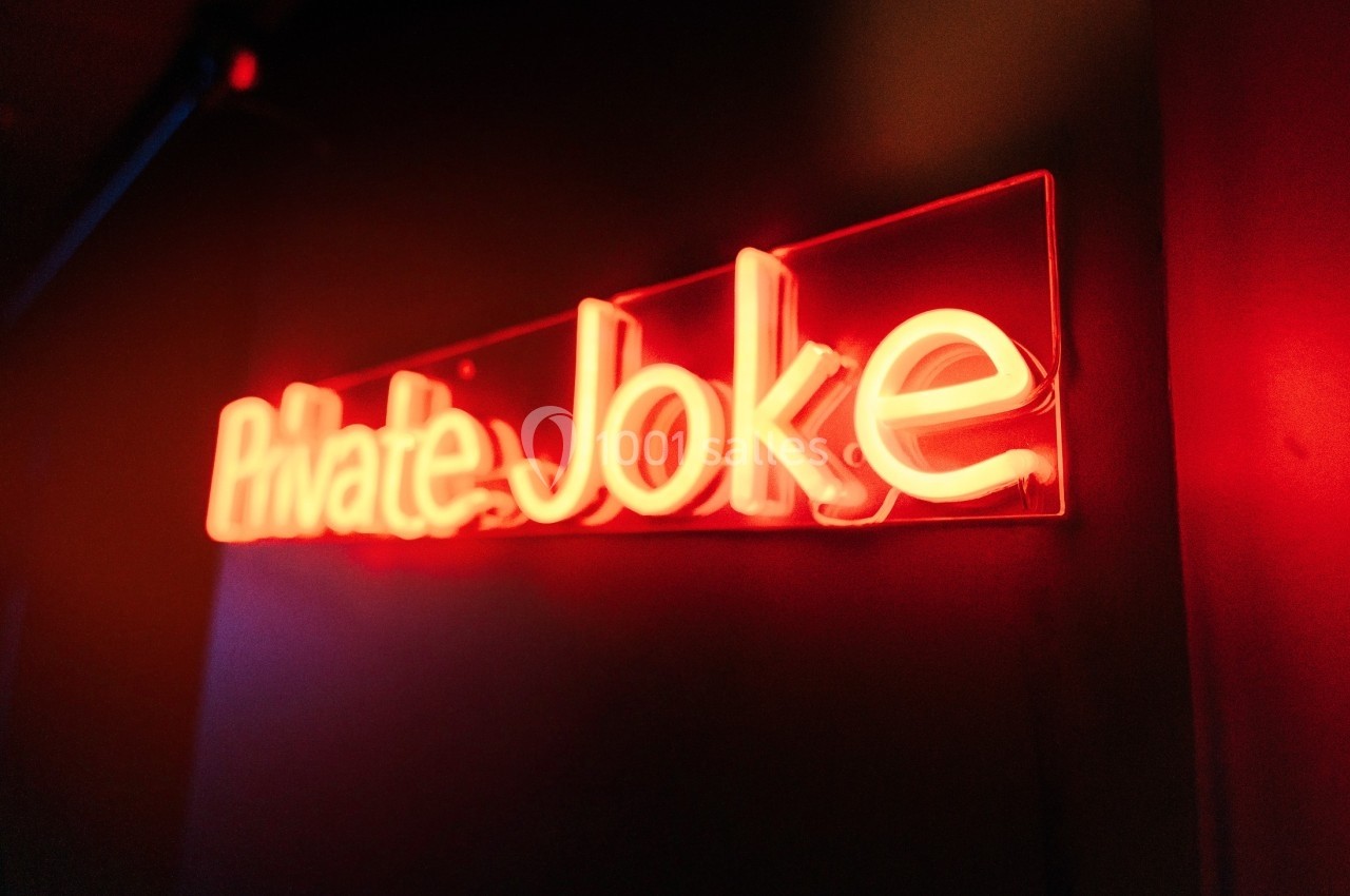 Enseigne lumineuse rouge avec l'inscription ’Private Joke’ dans un environnement sombre.