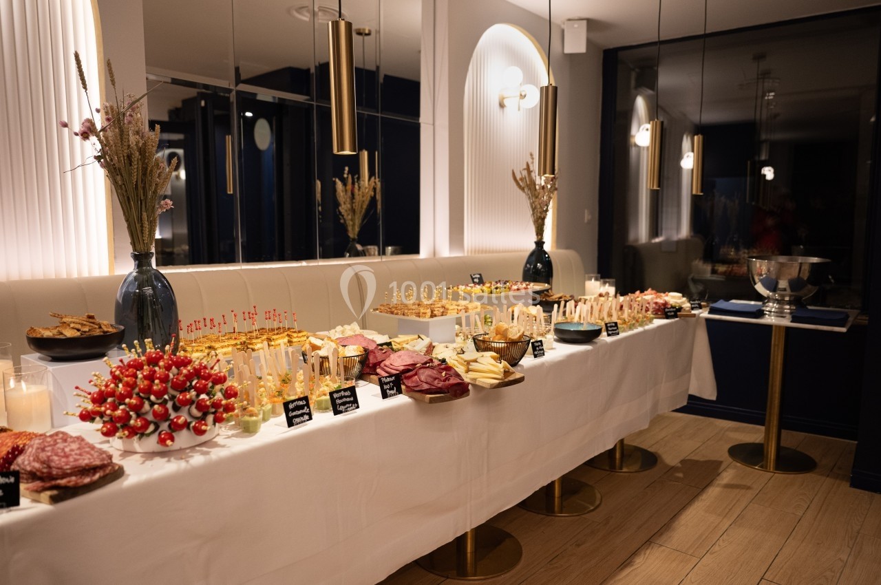 Buffet élégant avec une variété de plats, incluant brochettes, charcuteries et desserts, dans une salle moderne et lumineuse.