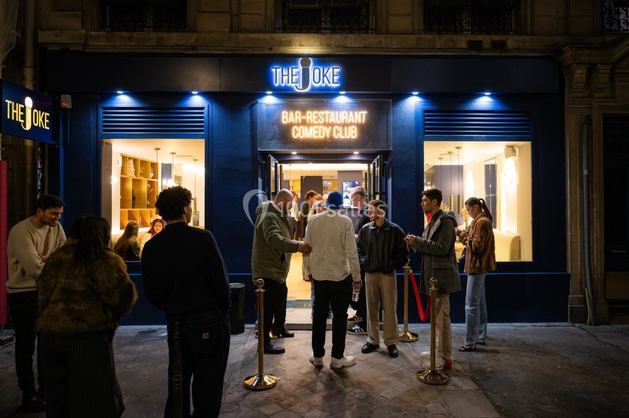 Façade d'un bar-restaurant avec enseigne lumineuse, des clients discutent devant l'entrée en soirée.