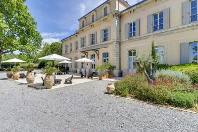 Grande table dressée en extérieur avec des chaises en bois, sous une pergola illuminée de lumières violettes, devant un…