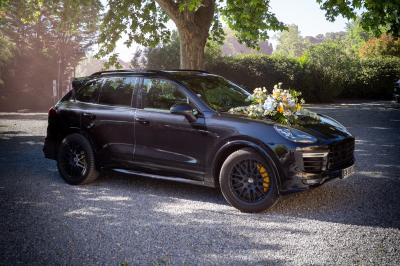 Grande table dressée en extérieur avec des chaises en bois, sous une pergola illuminée de lumières violettes, devant un…