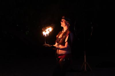 Grande table dressée en extérieur avec des chaises en bois, sous une pergola illuminée de lumières violettes, devant un…