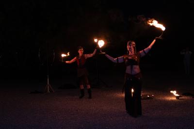 Grande table dressée en extérieur avec des chaises en bois, sous une pergola illuminée de lumières violettes, devant un…