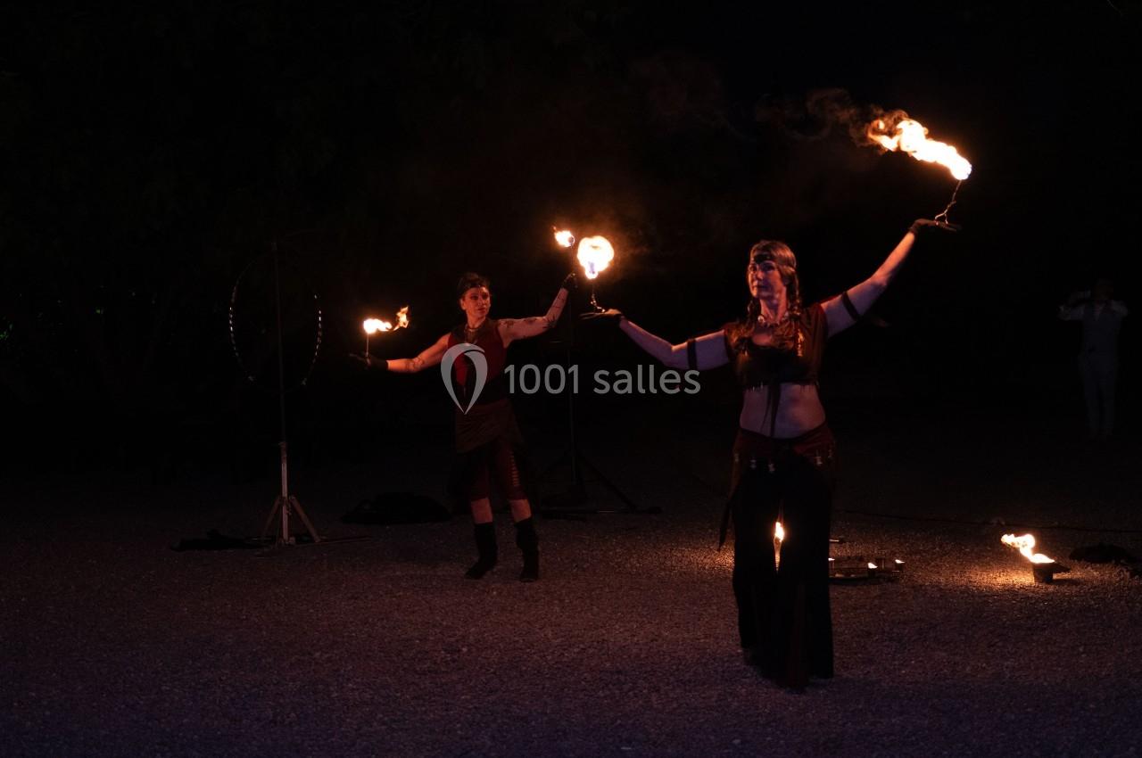 Deux artistes réalisent une performance nocturne avec des torches enflammées dans un espace extérieur sombre.