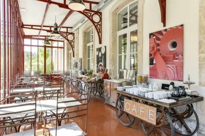 Grande table dressée en extérieur avec des chaises en bois, sous une pergola illuminée de lumières violettes, devant un…