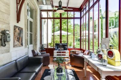 Grande table dressée en extérieur avec des chaises en bois, sous une pergola illuminée de lumières violettes, devant un…