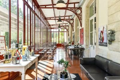 Grande table dressée en extérieur avec des chaises en bois, sous une pergola illuminée de lumières violettes, devant un…