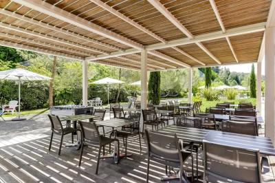 Grande table dressée en extérieur avec des chaises en bois, sous une pergola illuminée de lumières violettes, devant un…