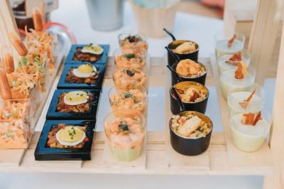 Grande table dressée en extérieur avec des chaises en bois, sous une pergola illuminée de lumières violettes, devant un…