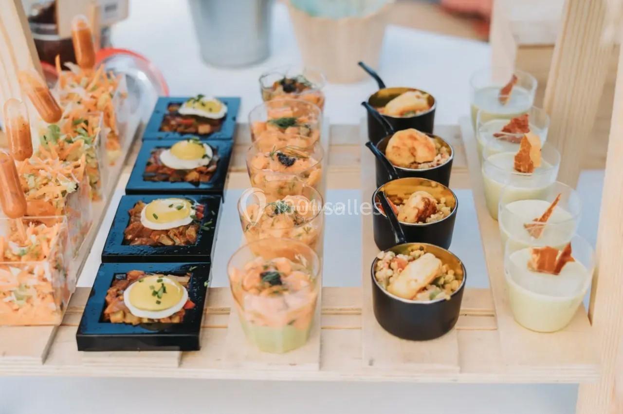 Plateau de verrines et bouchées variées, incluant légumes, œufs, crevettes et garnitures, présenté sur une table en bois.