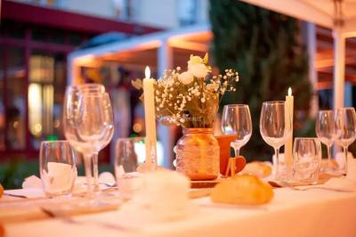 Grande table dressée en extérieur avec des chaises en bois, sous une pergola illuminée de lumières violettes, devant un…