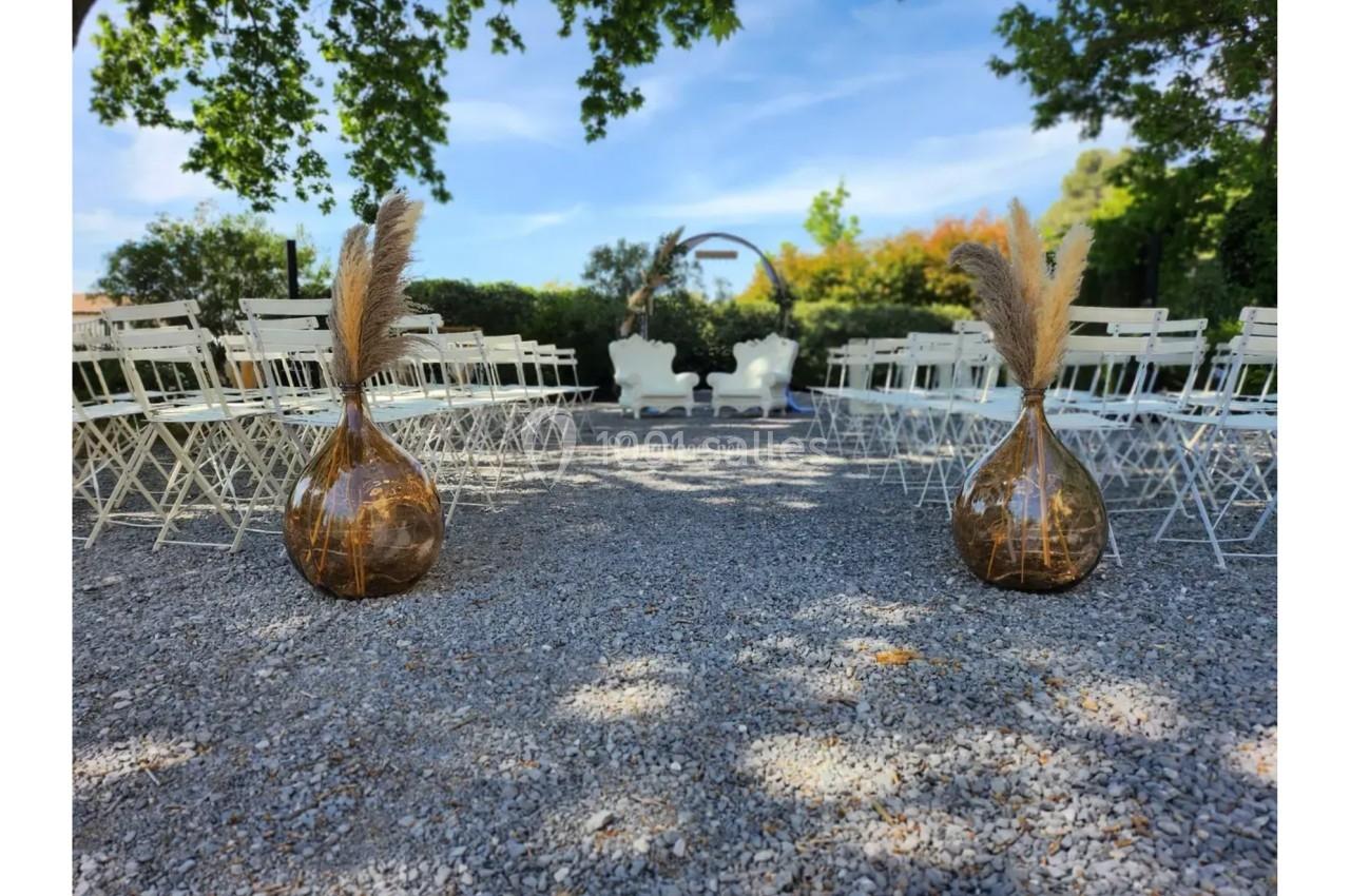 Allée centrale d'une cérémonie en extérieur, bordée de chaises blanches et décorée de vases avec des pampas.
